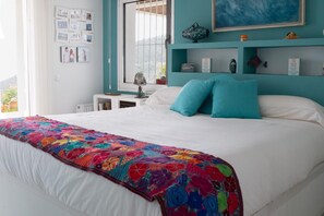 A bedroom with a bed, a colorful quilt, a window with a view, and a shelf with decorative items. - Vacation Villa With sea Views in Mojacar (Mojacar)
