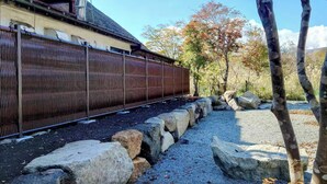 A train track with a metal fence, rocks, and trees in the background. - SAKURAHOTEI (Hakone)