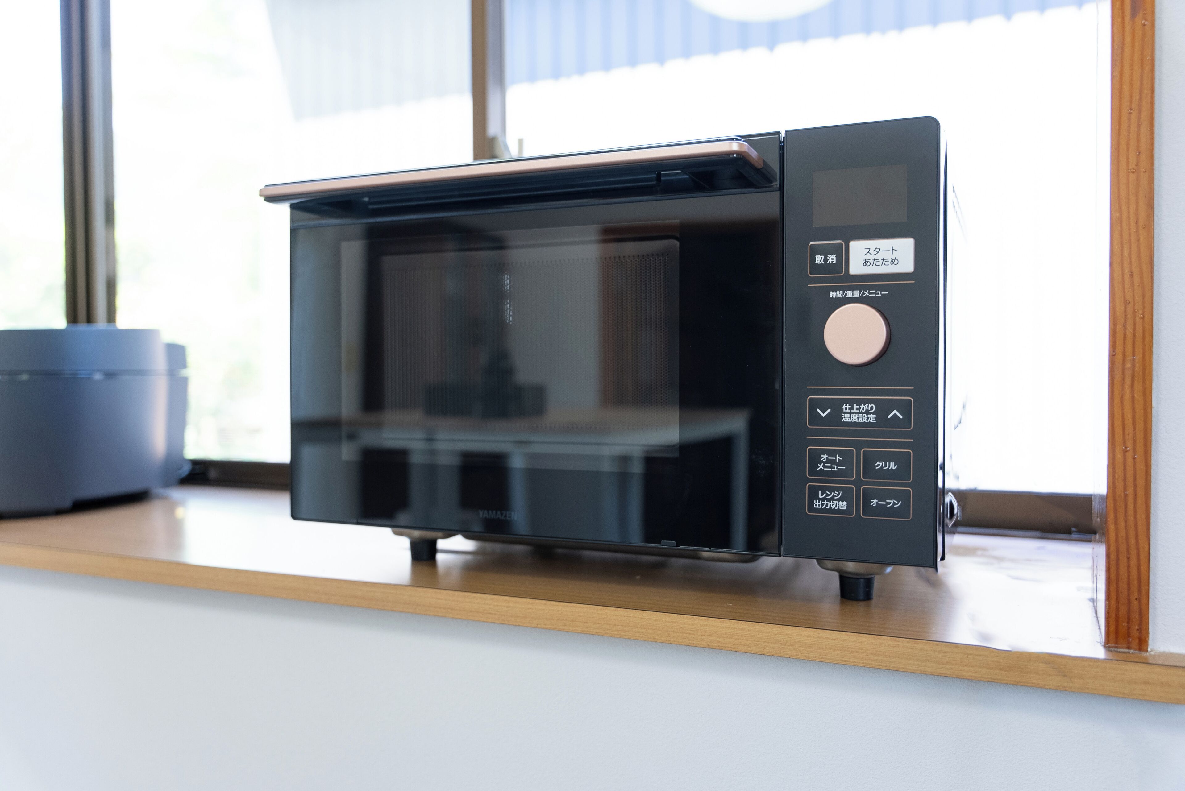 Un four à micro-ondes moderne doté d’un écran numérique et d’un panneau de commande, placé sur un plan de travail en bois près d’une fenêtre.
