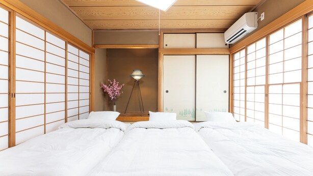 A traditional Japanese-style room with tatami flooring, a bed with white bedding, a floor lamp, and a sliding door. - SAKURAHOTEI (Hakone)
