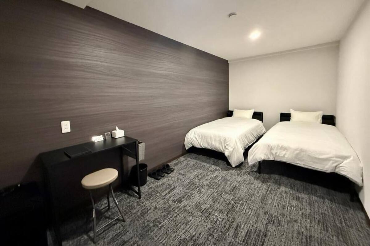 A modern hotel room with two beds, a desk, and a chair.