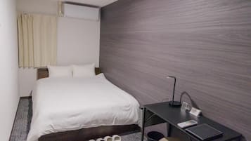 Habitación de hotel con cama, escritorio, silla, cesto de basura y un par de pantuflas.