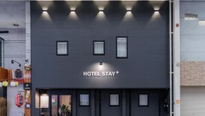 A modern hotel facade with a 'HOTEL STAY+' sign, large windows, and a dark exterior wall. - HOTEL STAY Plus (Imabari)