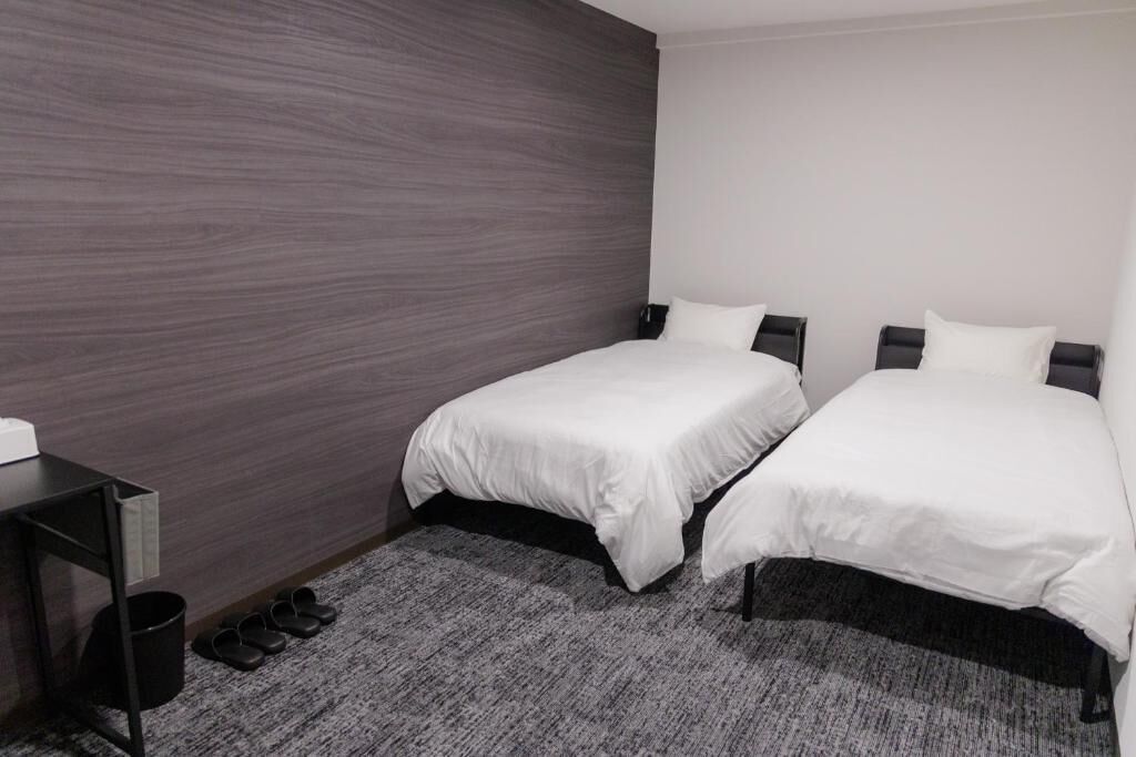 A hotel room with two beds, a desk, and a shoe rack.