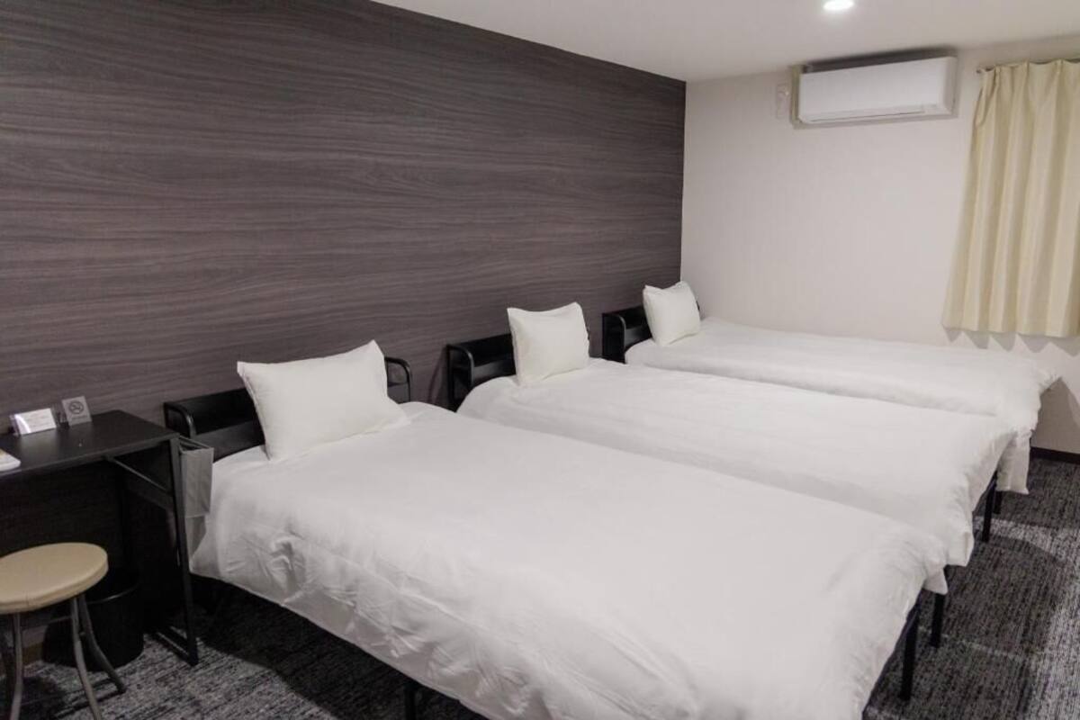 A hotel room with three single beds, a desk, a chair, and a small stool.