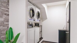A laundry room with two front-loading washing machines and a dryer, a small plant, and a door to another room. - HOTEL STAY Plus (Imabari)