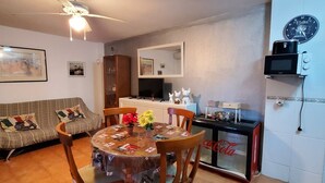 A dining area with a round table, chairs, a ceiling fan, a sofa, a kitchen area with a microwave, and a clock on the wall. - Nice Apartment in Natura World, Almeria (Vera)