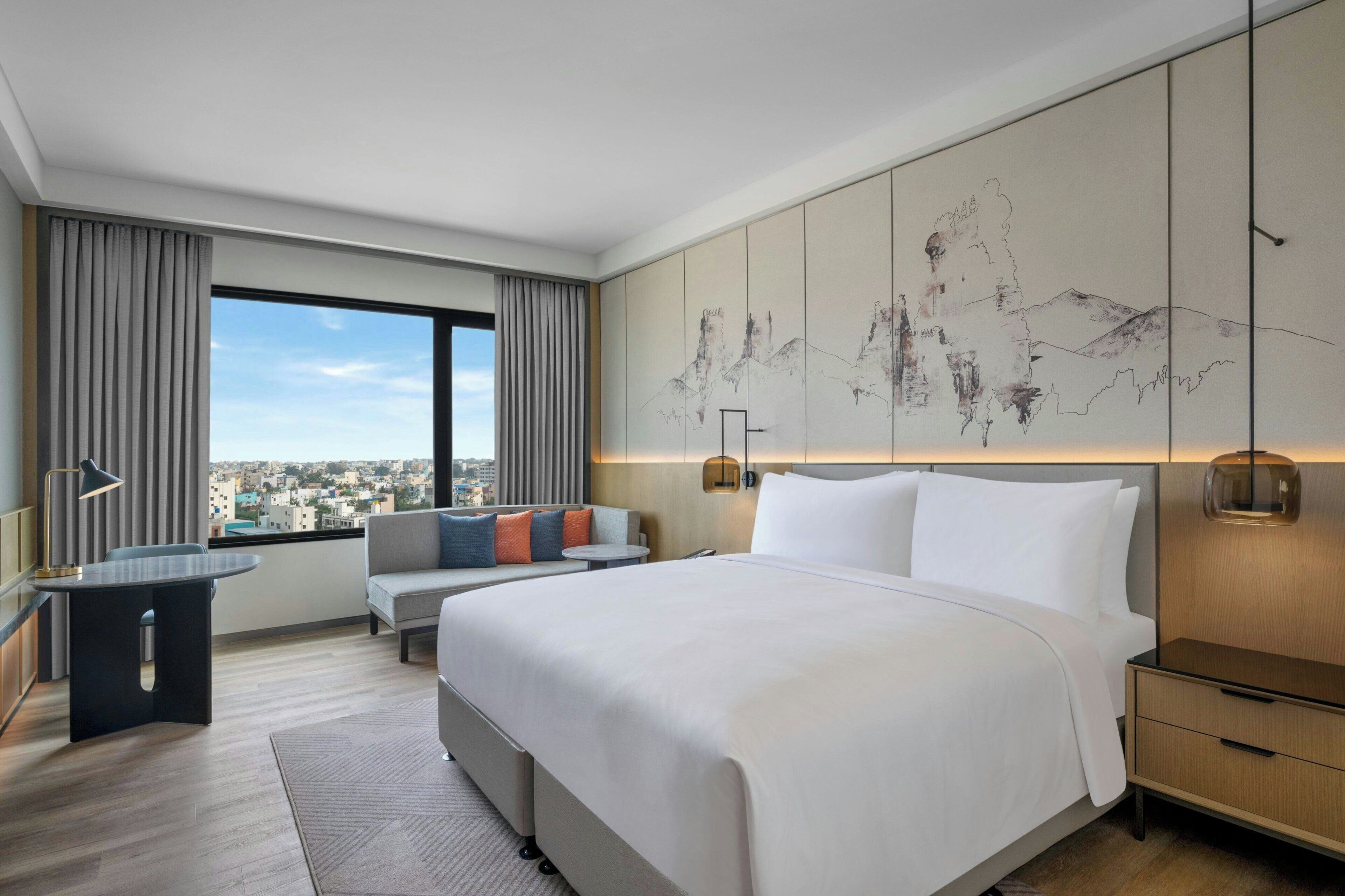 Una habitación de hotel moderna con una cama grande, un escritorio, un sofá y vistas a la ciudad.