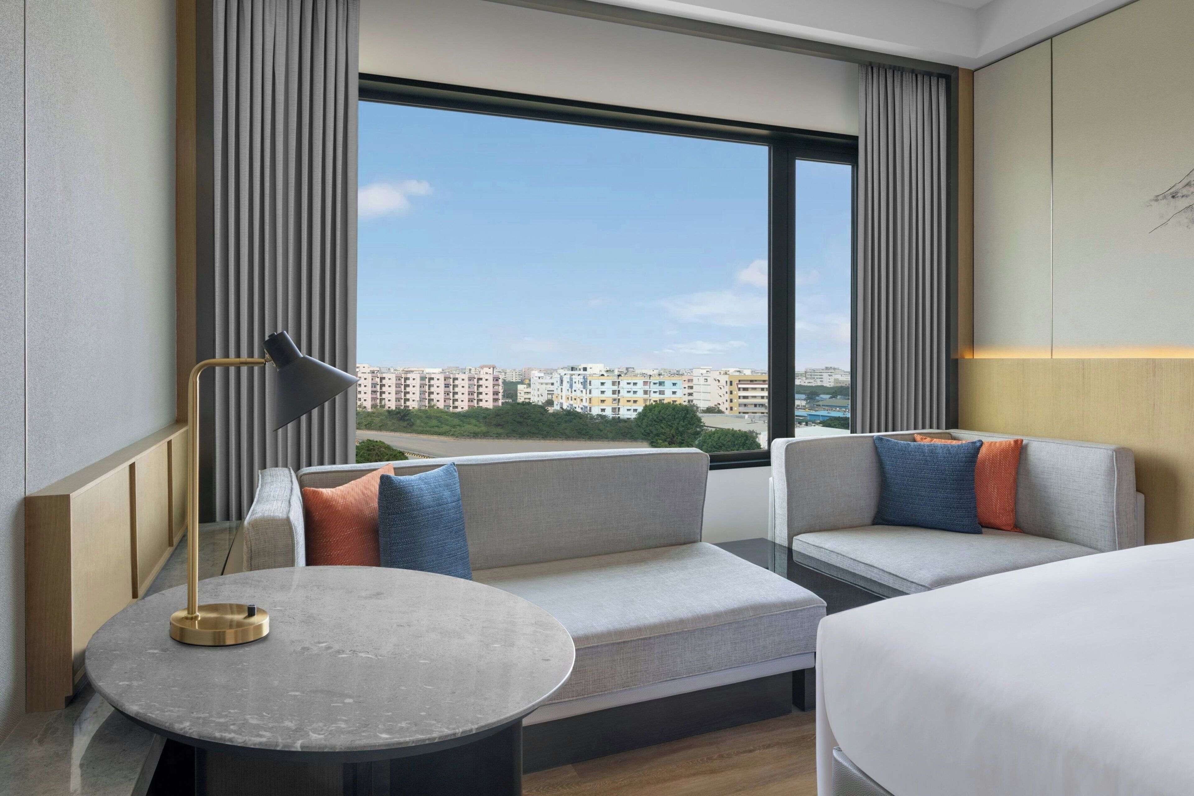 A hotel room with a large window, a sofa, a round table, and a bed.