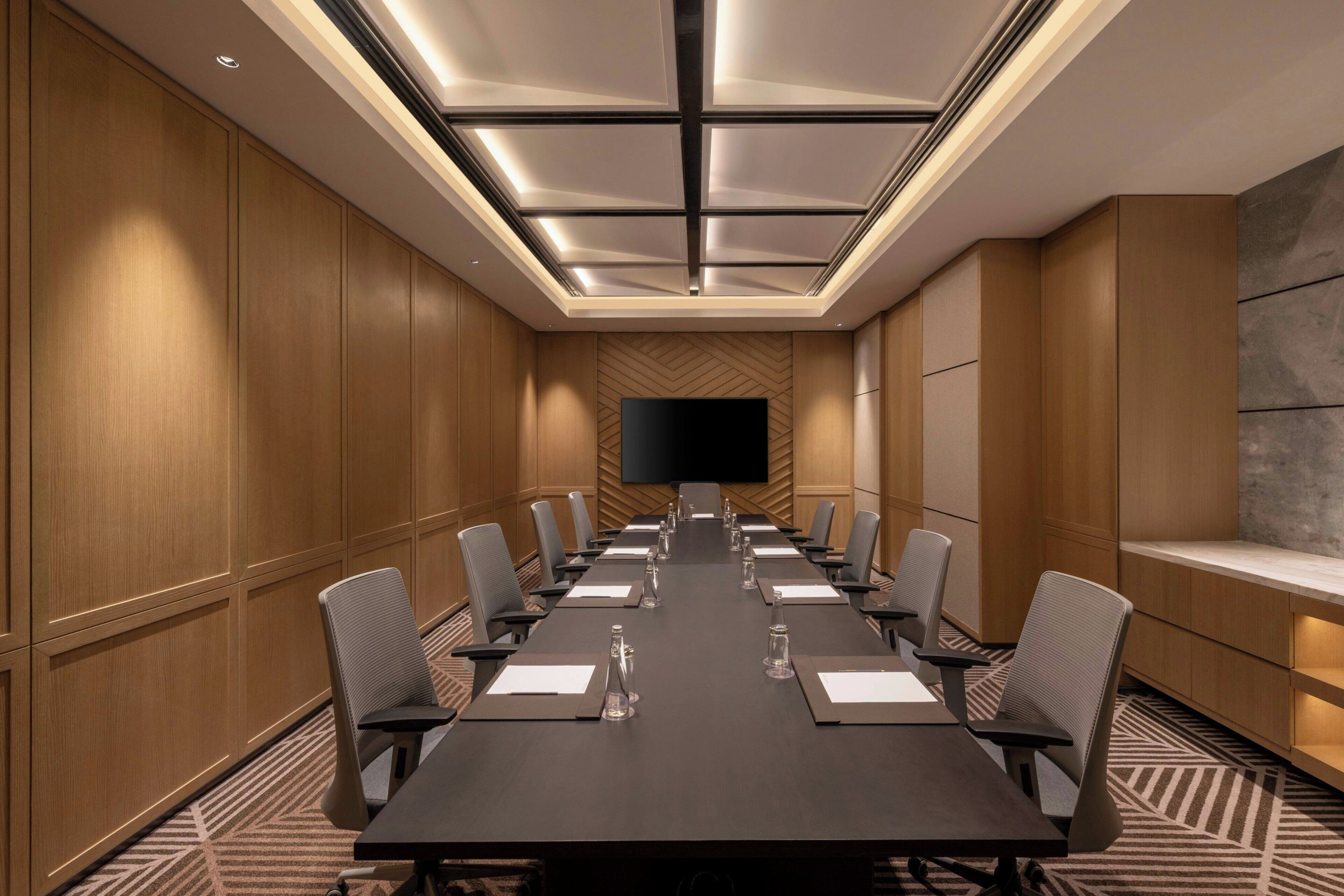 Un salón de conferencias con una larga mesa, sillas, un televisor de pantalla plana y paneles de madera.