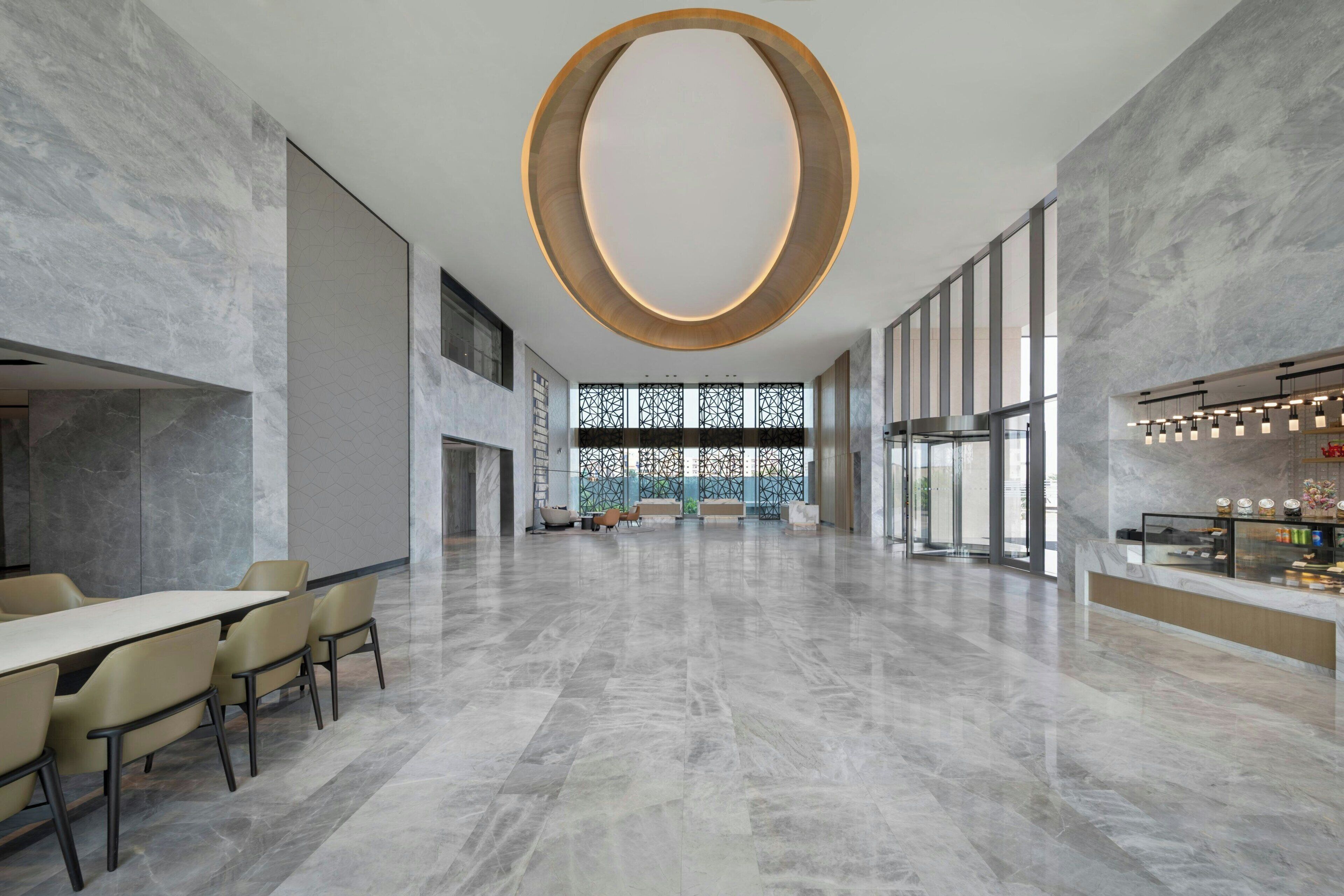 A spacious lobby with a large circular light fixture, a reception desk, and a seating area with chairs and a table.