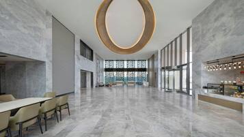 A spacious lobby with a large circular light fixture, a reception desk, and a seating area with chairs and a table.