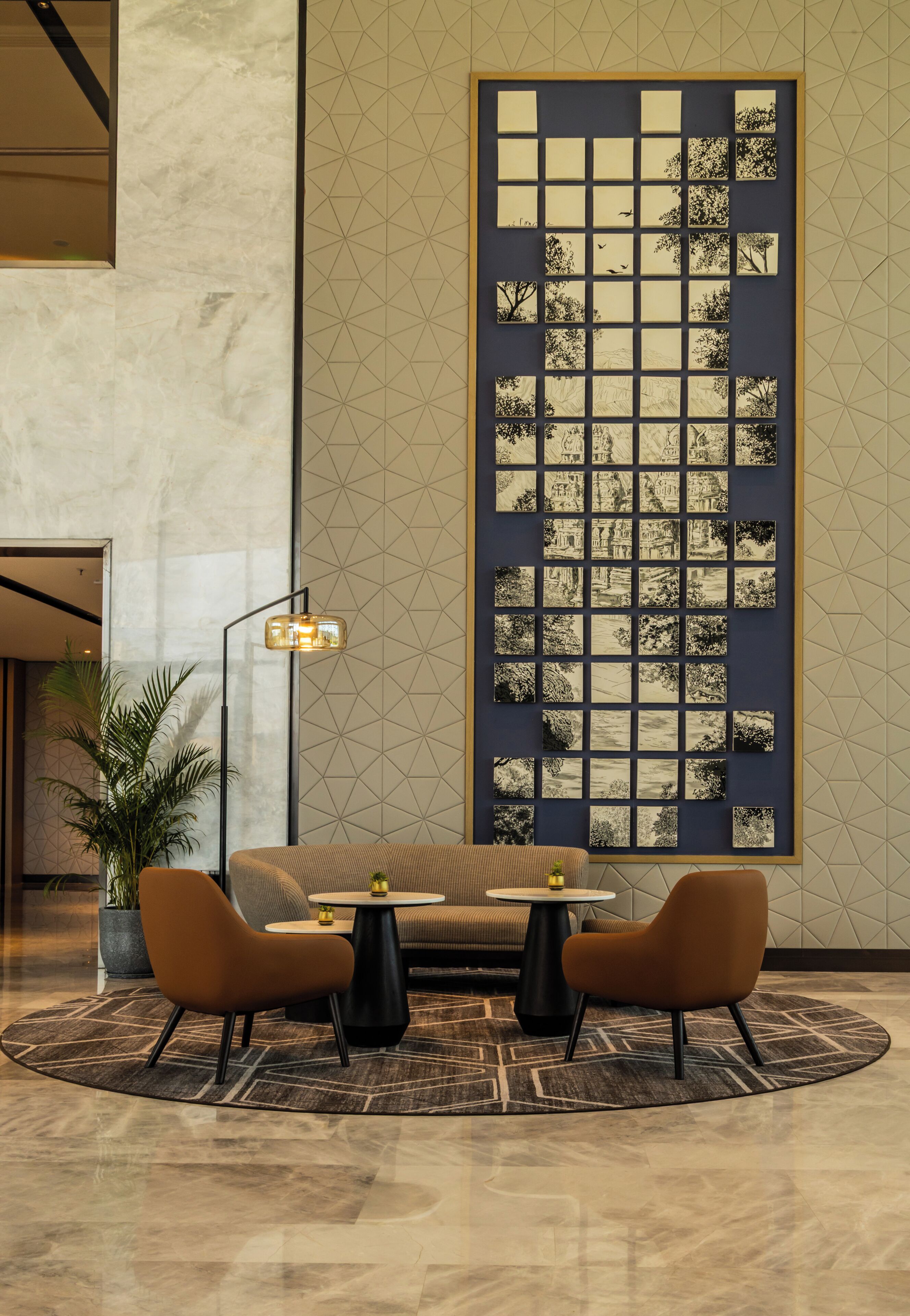 A modern lobby with a large wall art piece, a sofa, two armchairs, a coffee table, a floor lamp, and a potted plant.
