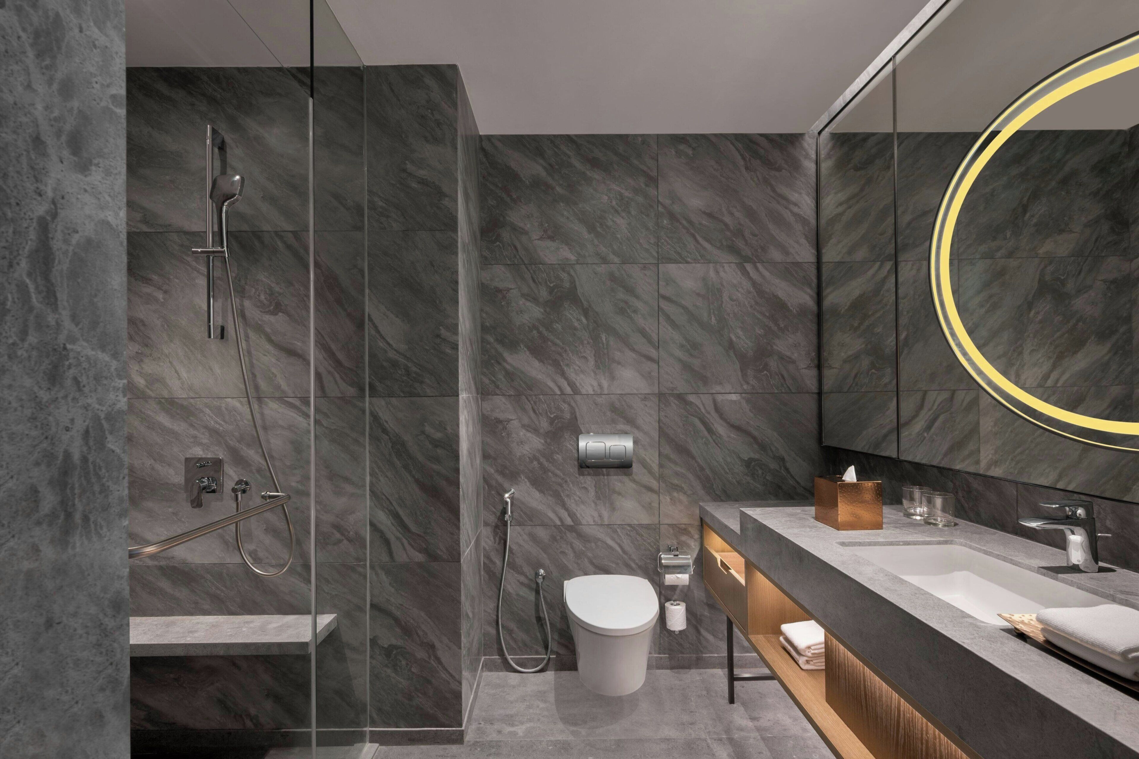 Un bagno moderno con cabina doccia in vetro, un mobile lavabo e uno specchio grande con cornice circolare.
