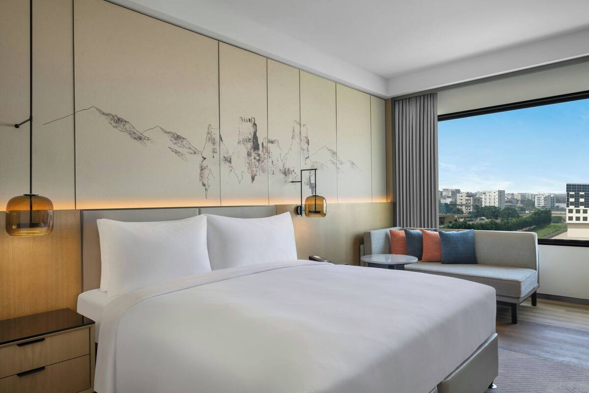 A hotel room with a large bed, a sofa, a small table, and a city view.