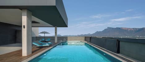 Una piscina en la azotea con vistas a montañas, sillas de descanso y una terraza de madera.