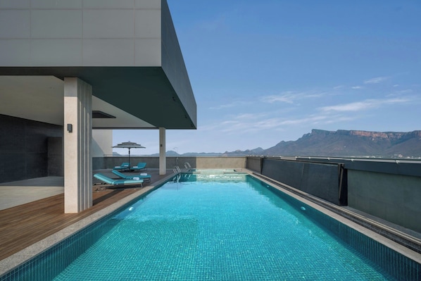 Piscina no terraço com vista para montanhas, cadeiras de lounge e deck de madeira.