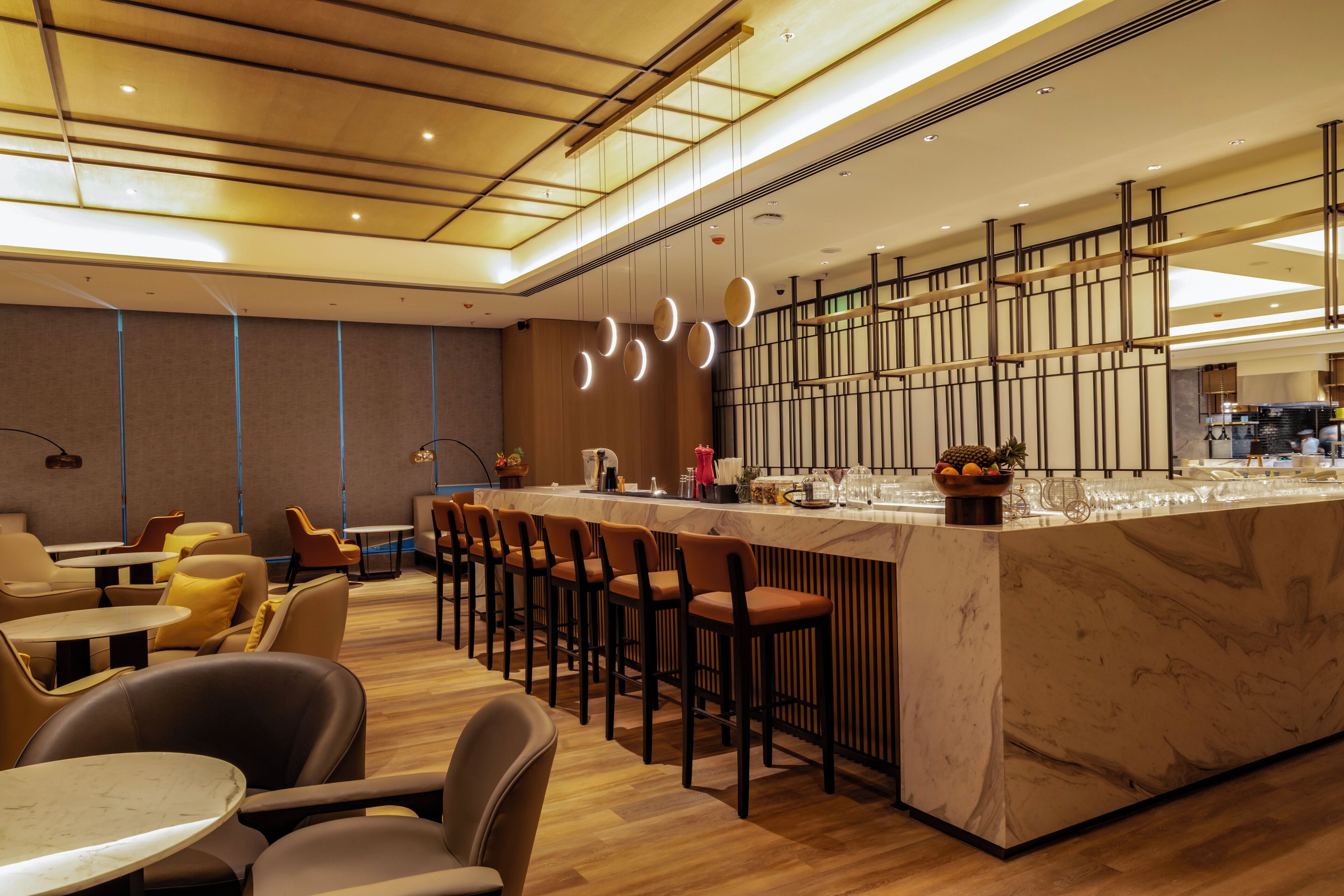 A modern bar area with a marble countertop, multiple bar stools, and pendant lighting.