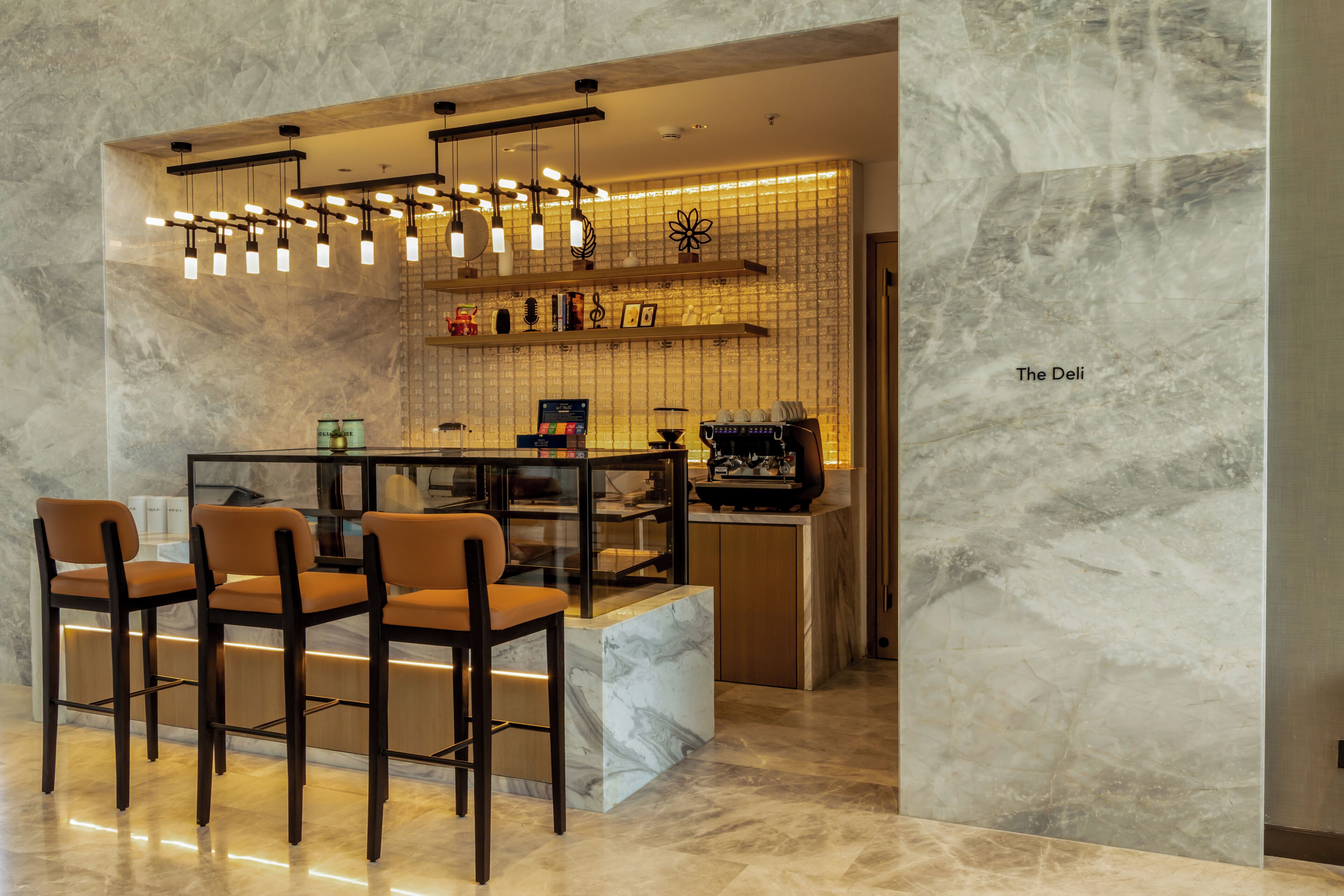 Zona de bar moderna con paredes de mármol, un separador de cristal y varias lámparas colgantes.