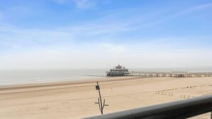 Una playa con un muelle largo que se extiende al mar, un edificio al final del muelle, y cielo despejado.