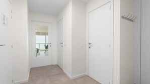 Un pasillo con una puerta que da a un balcón, un perchero y una pared lisa.