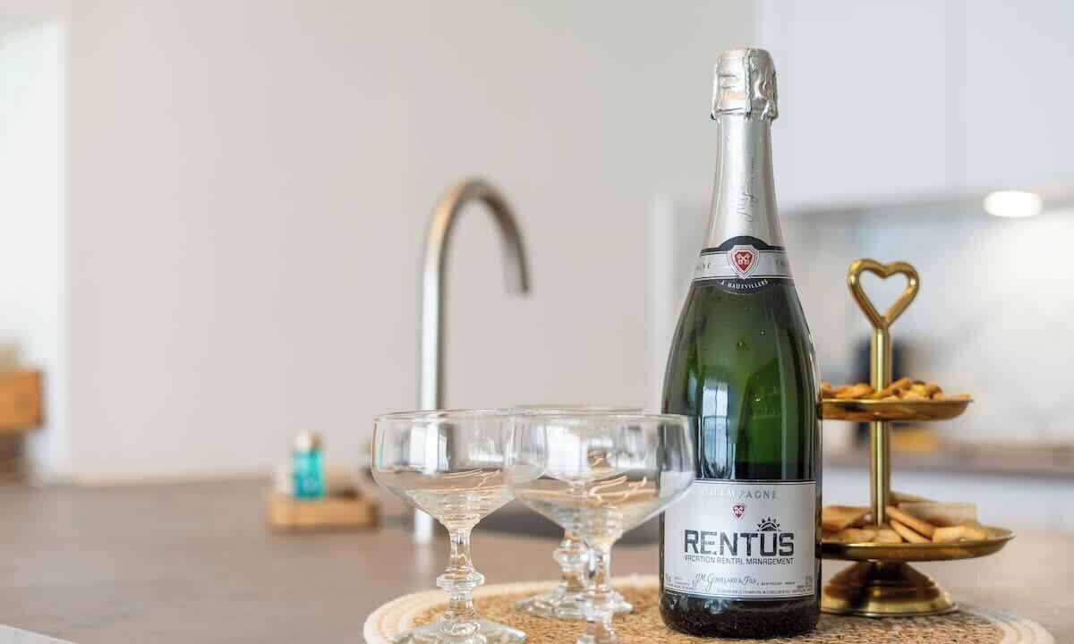 Une bouteille de champagne, deux verres vides et une décoration en forme de cœur, dorée, posée sur une table.