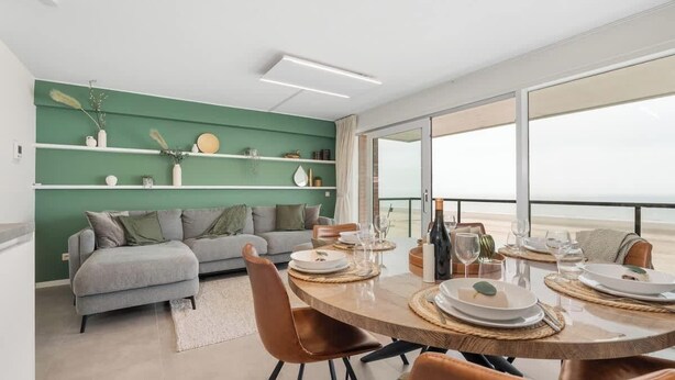 Un comedor moderno con una mesa redonda, sillas y una pared verde con estanterías.