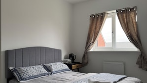 Un dormitorio con cama, mesita de noche, ventana con cortinas y radiador.
