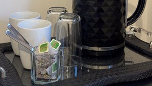 Una tetera con estampado de rombos negros, dos tazas blancas y un recipiente de vidrio con bolsitas de té sobre una bandeja negra.