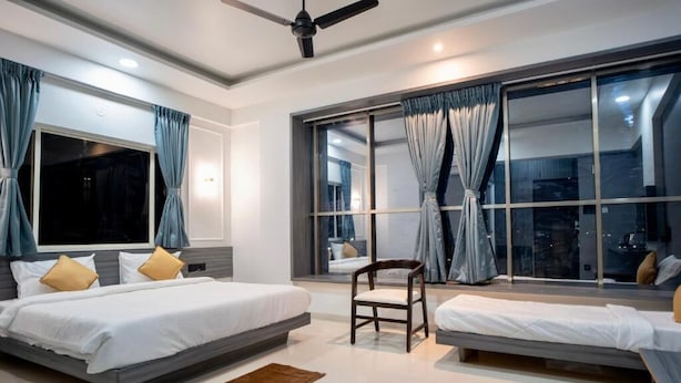 Une chambre moderne avec un grand lit, un plus petit lit, une chaise et une grande fenêtre avec des rideaux.