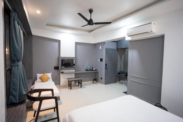 Ein modernes Hotelzimmer mit einem Bett, einem Schreibtisch, einem Sessel, einem Fernseher, einer Klimaanlage und einem Kleiderschrank.