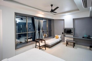 A modern hotel room with a large window, a bed, a chair, a small table, and a TV. - HOTEL OBERON (Solapur)