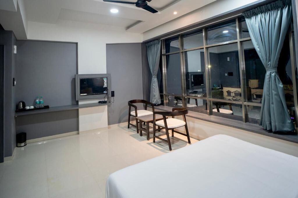 Habitación de hotel con cama, escritorio con silla, televisor y un ventanal con cortinas.