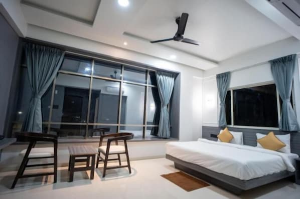 A modern hotel room with a large bed, two chairs, a table, and a ceiling fan.