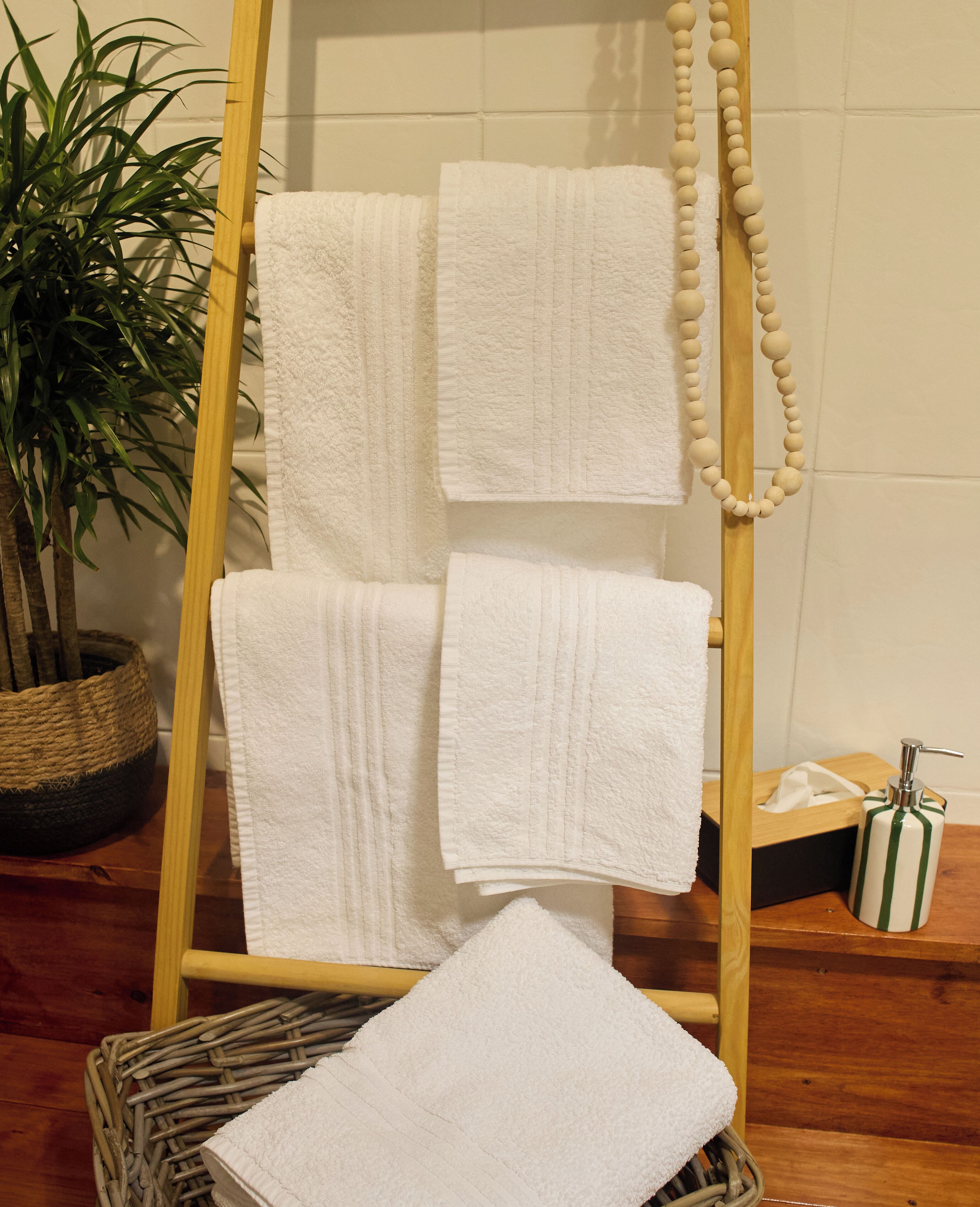 A wooden towel rack with three towels, a potted plant, a wicker basket, and a soap dispenser.
