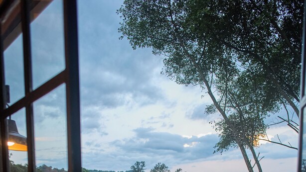 Una terraza de madera con una mesa y bancos, rodeada por una barandilla, con vistas a un paisaje boscoso.