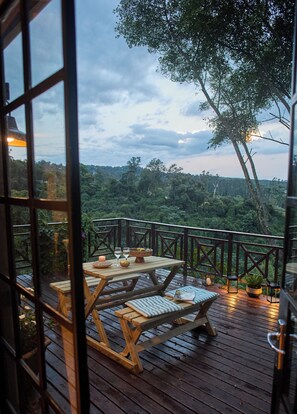 Une terrasse en bois, agrémentée d’une table et de bancs, entourée d’une rambarde et offrant une vue sur un paysage boisé.