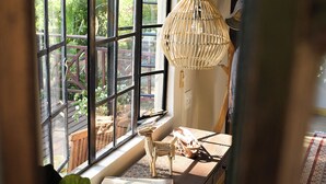 Una habitación con un ventanal grande, una lámpara de mimbre, una silla de madera y una mesa con diversos objetos.