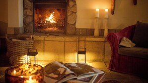 Una chimenea de piedra con fuego, un sofá rojo, un cráneo de toro colgado en la pared y un candelabro con velas.