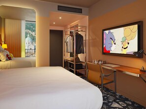 A hotel room with a bed, a desk, a chair, a TV, and a clothing rack. - Mama Shelter Lake Como (Como)