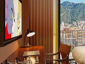 A hotel room with a wooden desk, a laptop, a chessboard, a lamp, a bed, and a large window with a city view. - Mama Shelter Lake Como (Como)