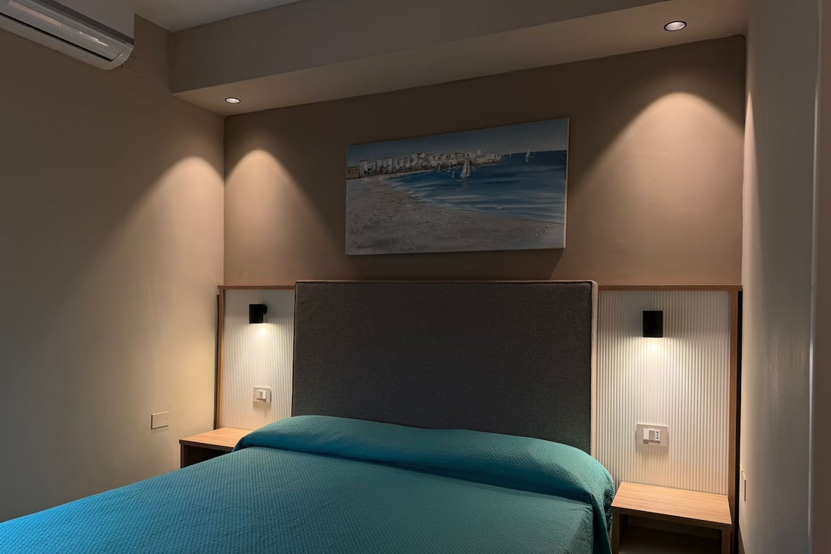 A bedroom with a bed, a painting, and a nightstand.