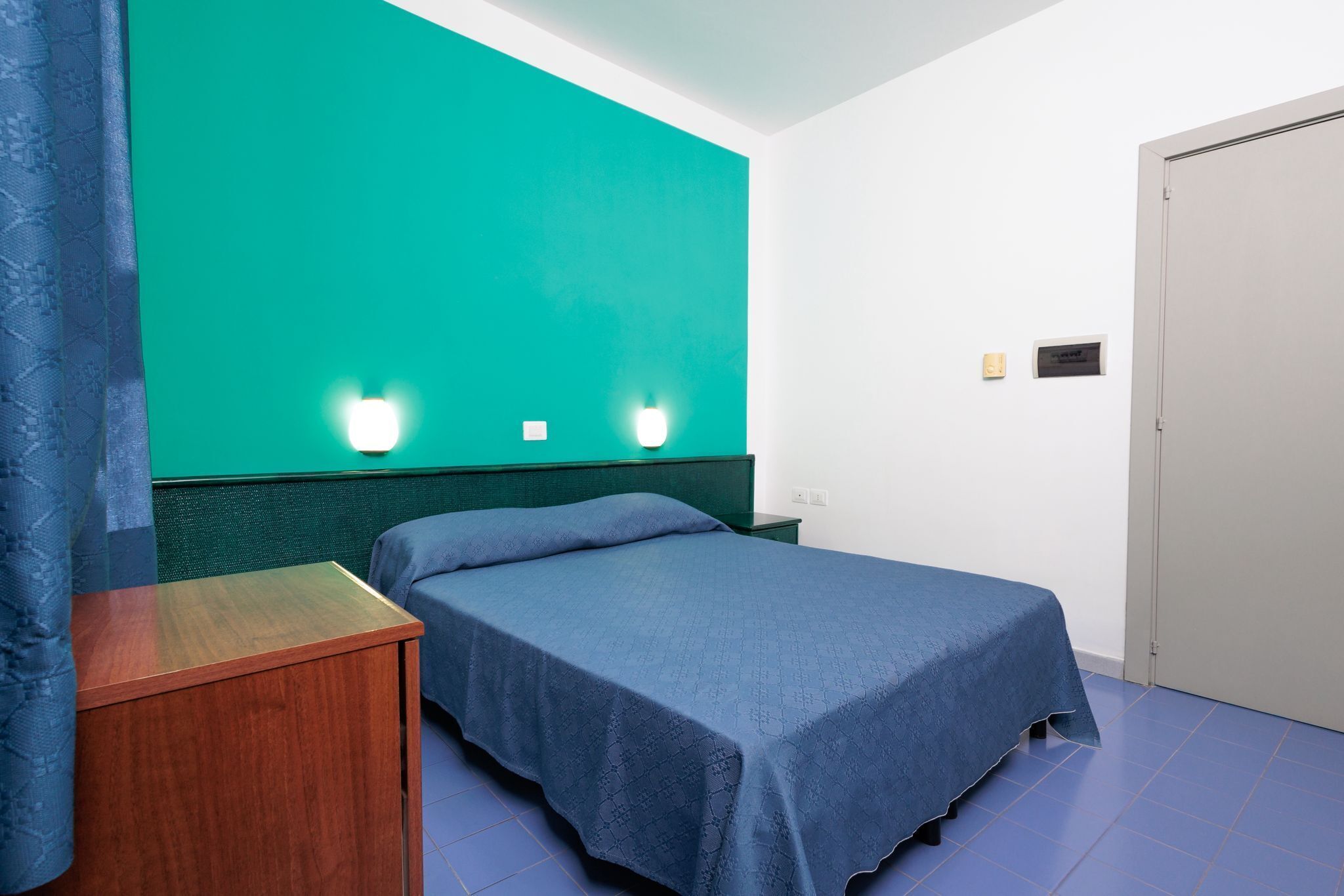 A room with a bed, a nightstand, a green wall, and a door.