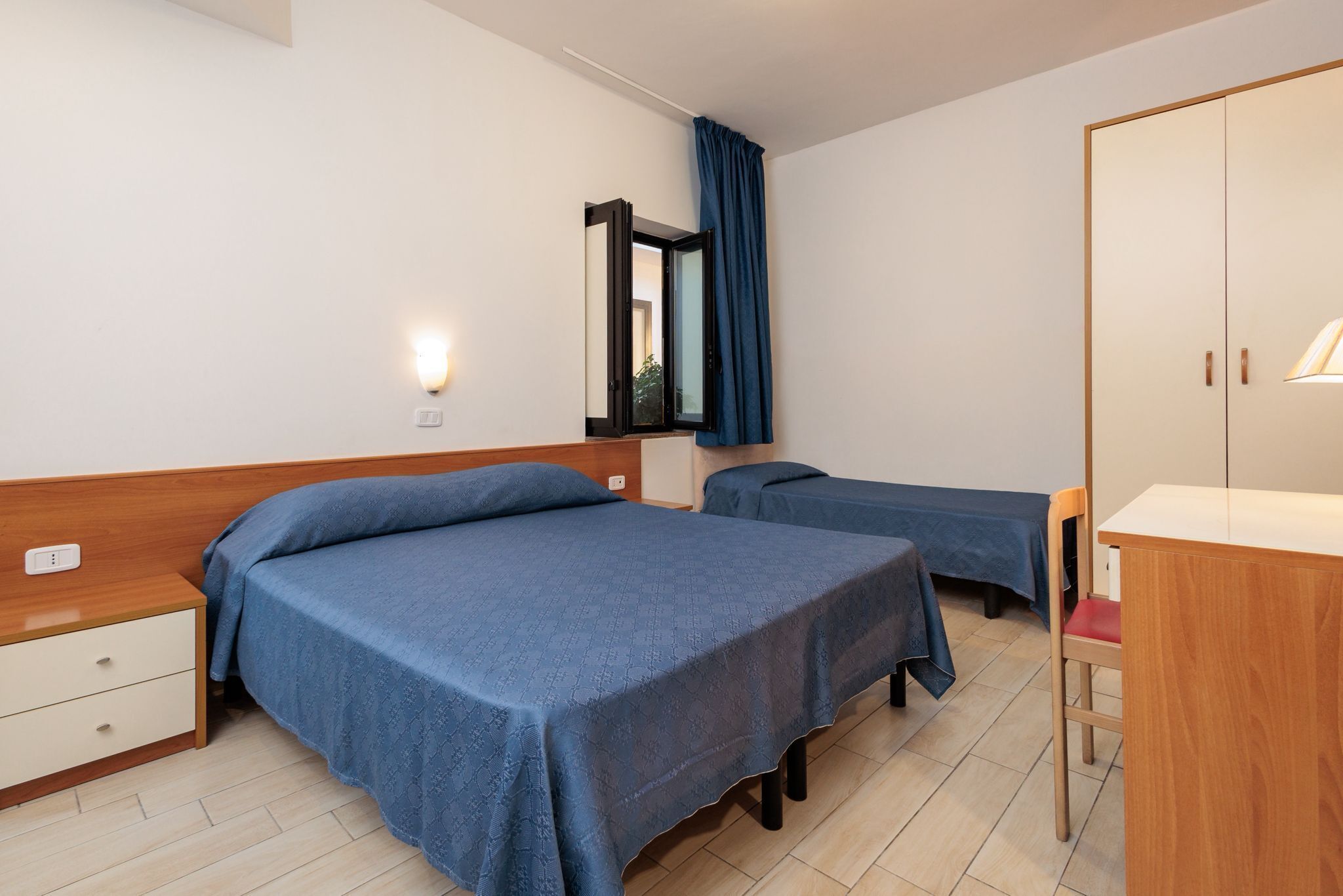 A bedroom with two beds, a desk, a chair, a wardrobe, and a mirror.