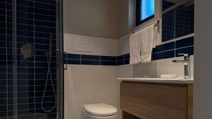 Une salle de bain moderne avec une douche à parois de verre, des toilettes, un lavabo avec un miroir et un porte-serviettes.