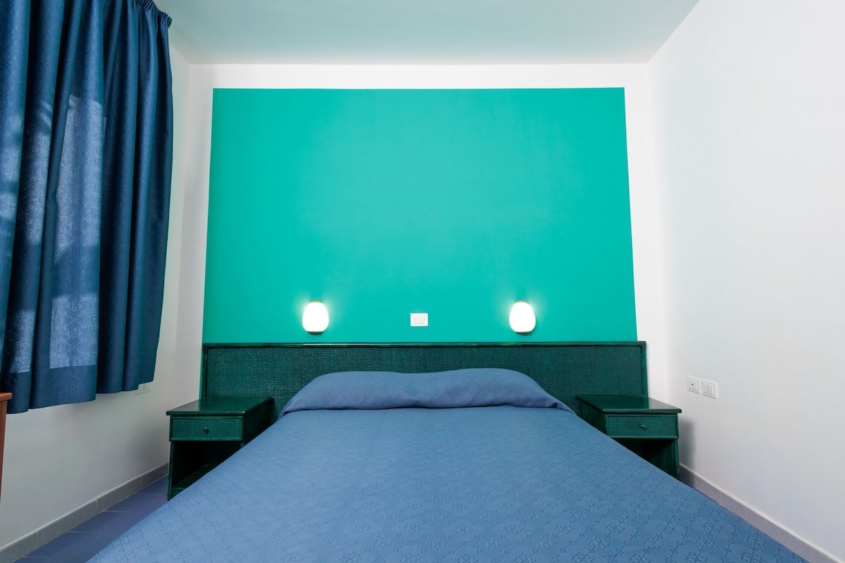 A room with a bed, two bedside tables, a green headboard, and a teal accent wall.