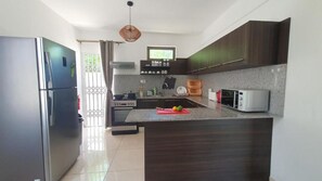 A modern kitchen with dark wooden cabinets, a stainless steel refrigerator, a microwave, and a large island with a red cutting board. - Beach Getaway - Duplex with Pool (Pereybere)