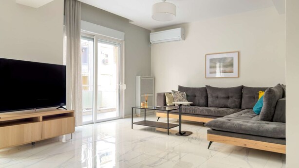 Ein modernes Wohnzimmer mit Flachbildfernseher, einem grauen Sofa, einem Couchtisch und einem großen Fenster.
