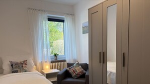 Een slaapkamer met een bed, een stoel, een kledingkast, een raam met gordijnen en een radiator.