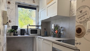 Een kleine keuken met een magnetron, koffieapparaat en bestek op het aanrecht.